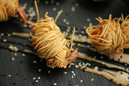 close up food photo of fried tiger prawns in egg noodles on black slate background. Asian culture and cuisine. Food image of shrimps for design of cafe, restaurant, menu.の写真素材