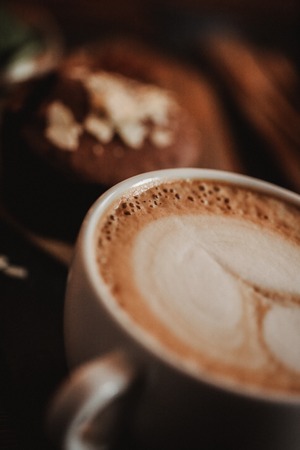 Close up food image of cup of coffee with picture on a foam on the wooden table background in cafe. Trend warm toning. Photo with a small depth of field.の写真素材