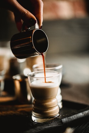 Hand of barista making making coffee in cafe. Cup of traditional espresso with milk. Coffee pouring into shot glasses. Toned image.の写真素材