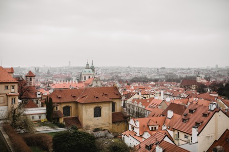 City of Prague with red roofs and Church in fog. City view of Praha old city. Rustic grey colors toning.の写真素材