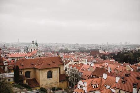 City of Prague with red roofs and Church in fog. City view of Praha old city. Rustic grey colors toning.の写真素材