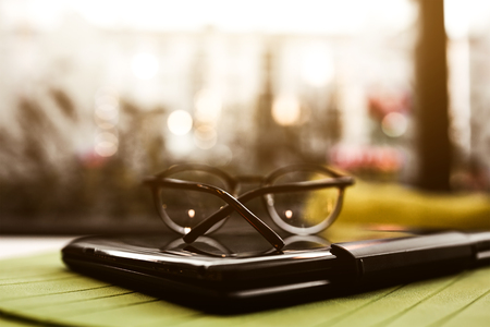 Modern glasses of businesswomann lying on notebook on table in cafe. Freelance working in restaurant. Business background. Flare copyspace for text and design.の写真素材