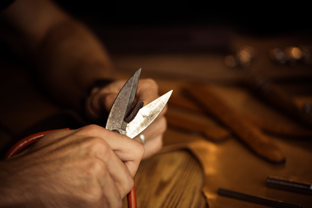 Working process of the leather belt in the leather workshop. Man holding crafting tool and working. Tanner in old tannery. Wooden table background. Close up man arm.の写真素材