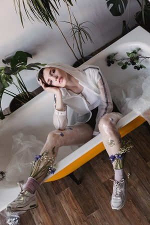 Fashion portrait of girl in plastic trend clothes. Eco styling. Model lying in bath.の写真素材