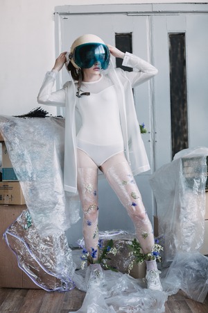Fashion portrait of girl in plastic trend clothes with space helmet on head. Eco styling. Model standing in poses.の写真素材