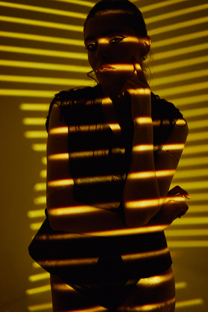 Beauty portrait of girl with light stripes and shadows in gold color. Hight quality retouching photo. Fashion glamour model.の写真素材