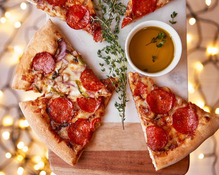 Christmas and New Year atmosphere. Hot Italian pizza with melting tomato, pepperoni and cheese on a white marbel cutting board. Background with lights in bokeh and selective focus.の写真素材