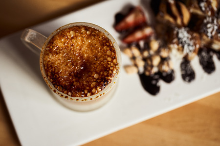 Macro photo of cup of Hot latte with baked caramel crust and sweet roll with banana and strawberry on the wooden table in coffe-sho. Coffee concept. Top view photo of two sets.の写真素材