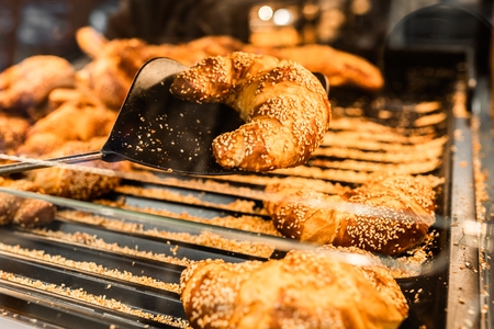 Fresh croissant on bread shelf in store. A man takes a fresh batch with a spatula. Food concept.の写真素材