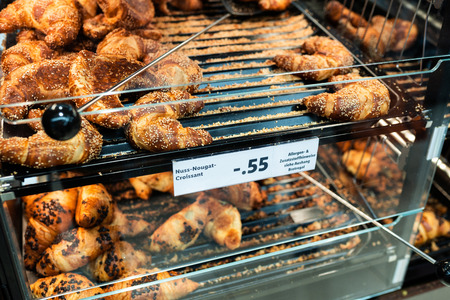 Fresh croissant on bread shelf in store with price. A man takes a fresh batch with a spatula. Food concept.の写真素材