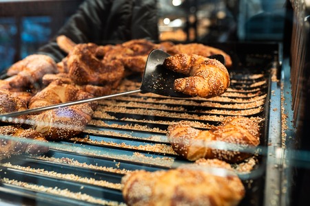 Fresh croissant on bread shelf in store. A man takes a fresh batch with a spatula. Food concept.の写真素材
