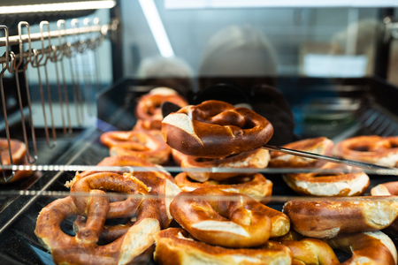 Germany national bakery - brezel. Fresh pretzel on bread shelf in store. Take a fresh bavarian Brezel with a spatula. Breakfast food concept.の写真素材