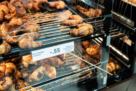 Fresh croissant on bread shelf in store with price. A man takes a fresh batch with a spatula. Food concept.の写真素材