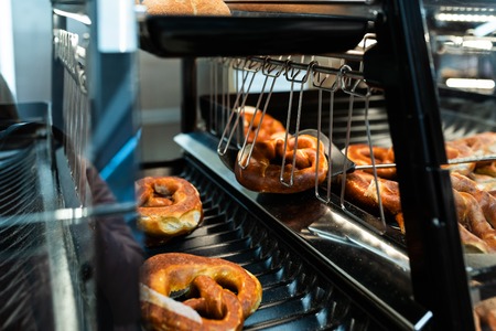 Germany national bakery - brezel. Fresh pretzel on bread shelf in store. Take a fresh bavarian Brezel with a spatula. Breakfast food concept.の写真素材