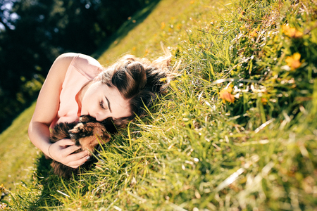 Girl lying on grass with cat. Spring or summer warm weather concept. Bokeh background. Ginger kitten with two face color mask.の写真素材