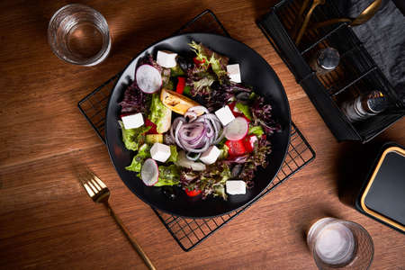 Fresh greek salad with tomato, radish, onion, bel pepper , olives and feta cheese on black plate, top view, wooden backgroundの写真素材