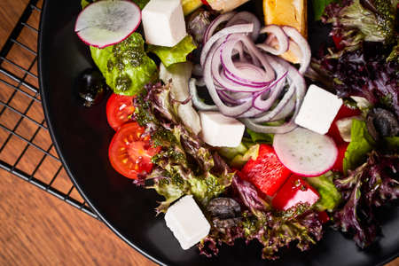 Fresh greek salad with tomato, radish, onion, bel pepper , olives and feta cheese on black plate, top view, wooden backgroundの写真素材