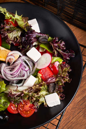 Fresh greek salad with tomato, radish, onion, bel pepper , olives and feta cheese on black plate, top view, wooden backgroundの写真素材