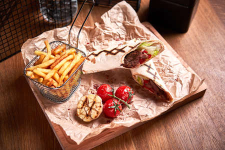 Turkish Shawarma with beef and fried with tomatoes on craft paper on wooden plate. Fast food set. Side viewの写真素材