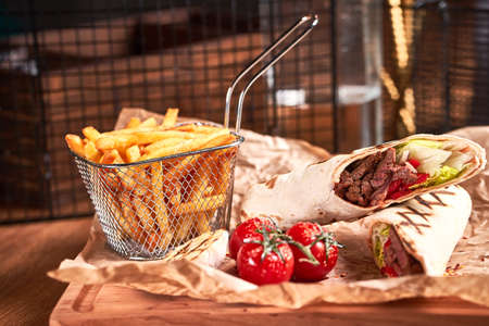 Turkish Shawarma with beef and fried with tomatoes on craft paper on wooden plate. Fast food set. Side viewの写真素材
