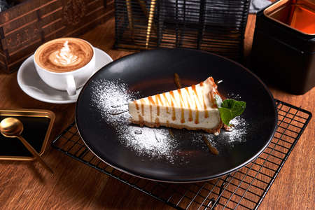 Piece of Cheesecake on black plate on a table with mint and a cup of coffee. Side viewの写真素材