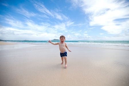 Excited toddler running away from the waves towards the camera on a tropical beach の写真素材