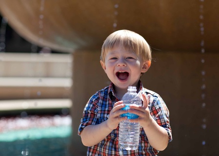 portrait of an adorable happy toddler holding a water bottle standing by a fountain outside