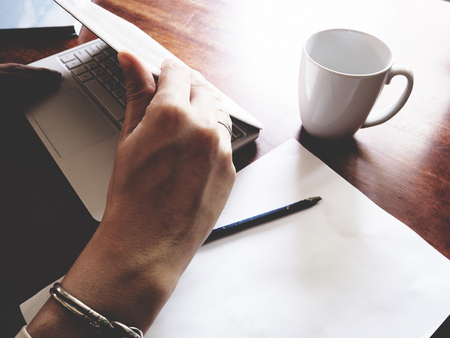 There are book, laptop, coffee cup, paper, and pencil on the office wooden  desk