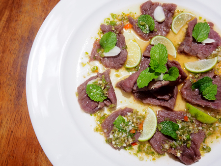 This is spicy beef salad in white plate above  woodenの写真素材