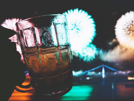 Hold a glass of beer near the river, can see blooming  fireworkの写真素材