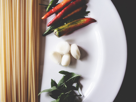 This is preparation for pasta dish, consist of dried linguine, garlic, chili and sweet basil on the white plate above wooden table, soft  toneの写真素材