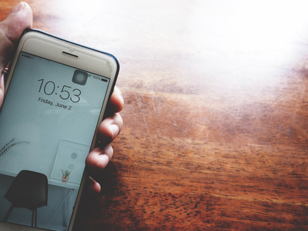Holding a smartphone above wooden table, showing date and time,  soft tone