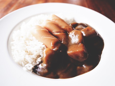 This is kare raisu (curry over rice) in white plate above wooden table,  soft toneの写真素材