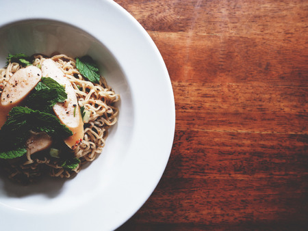 This is spicy noodles salad with sausage on wooden table,  soft toneの写真素材