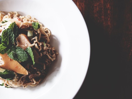 This is spicy noodles salad with sausage on wooden table,  soft toneの写真素材