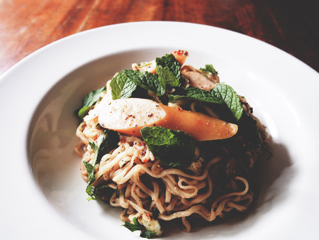 This is spicy noodles salad with sausage on wooden table,  soft toneの写真素材