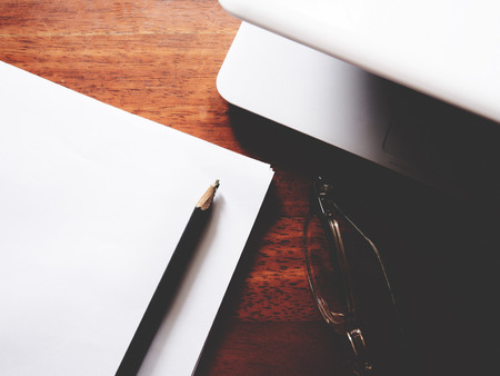 The picture of work space on wooden table, consist of glasses, paper, pencil and  laptop,  soft tone colorの写真素材