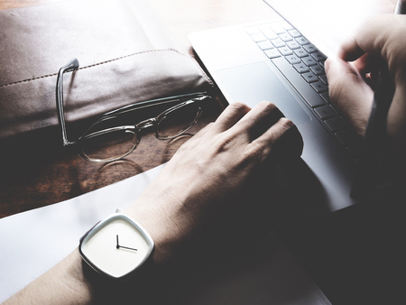 The picture of hands working action on wooden table, consist of laptop, paper, pencil, watch, glasses, soft tone colorの写真素材
