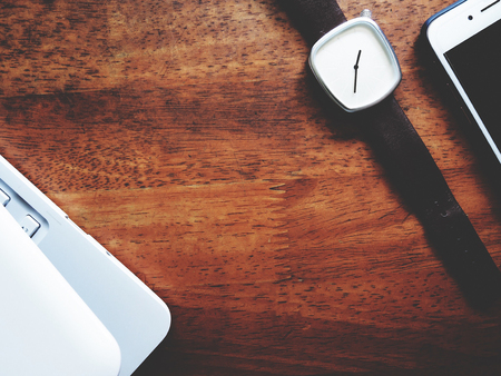 Top view picture of white laptop, watch and smartphone in minimal style above old wooden background....