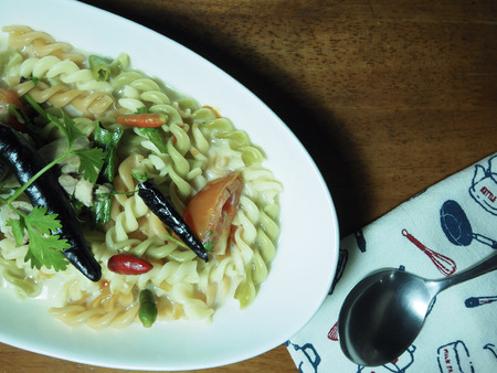 Top view picture of fusilli in coconut milk soup with chicken on white plate above old wooden table.  fusion foodの写真素材