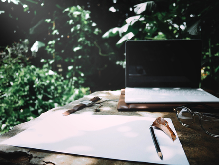 Businesses happen everywhere, just have inspiration. The picture of white laptop, paper, pencil, watch and glasses on green forest background in the afternoon.  selective focusの写真素材