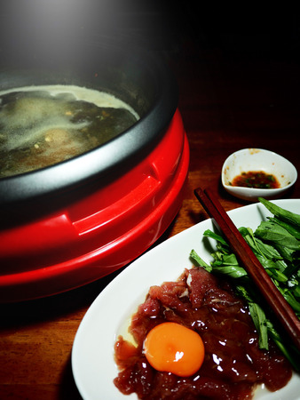 The picture of preparation sukiyaki consist of beef, egg, morning glory, hot pot, and sukiyaki sauce on old wooden table.  selective focusの写真素材