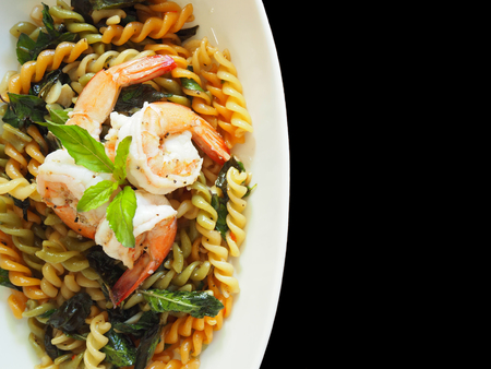 This is Thai - Italian fusion food dish. The picture of fusilli and shrimp with Thai basil in white dish on  black background.の写真素材