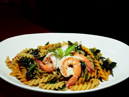 This is Thai - Italian fusion food dish. The picture of fusilli and shrimp with Thai basil in white dish on  black background.の写真素材