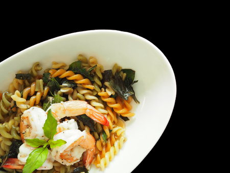 This is Thai - Italian fusion food dish. The picture of fusilli and shrimp with Thai basil in white dish on  black background.の写真素材