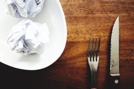 No work No money and No food. The picture of failed work condition consist of disastrously paper on white dish, pencil, fork, spoon, hand and knife above wooden table. selective focus. soft tone styleの写真素材