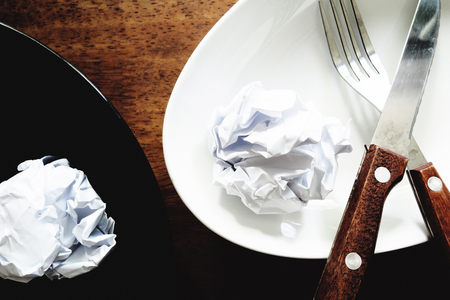 No work No money and No food. The picture of failed work condition consist of disastrously paper on white dish, pencil, fork, spoon, hand and knife above wooden table. selective focus. soft tone styleの写真素材