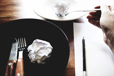 No work No money and No food. The picture of failed work condition consist of disastrously paper on white dish, pencil, fork, spoon, hand and knife above wooden table. selective focus. soft tone styleの写真素材