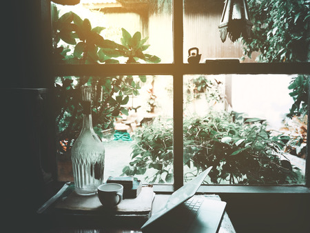 Businesses happen everywhere, just have inspiration. The picture of white laptop and a cup of coffee on wooden table near the window at home office. selective focusの写真素材