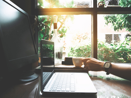Businesses happen everywhere, just have inspiration. The picture of white laptop and a cup of coffee on wooden table near the window at home office. selective focusの写真素材